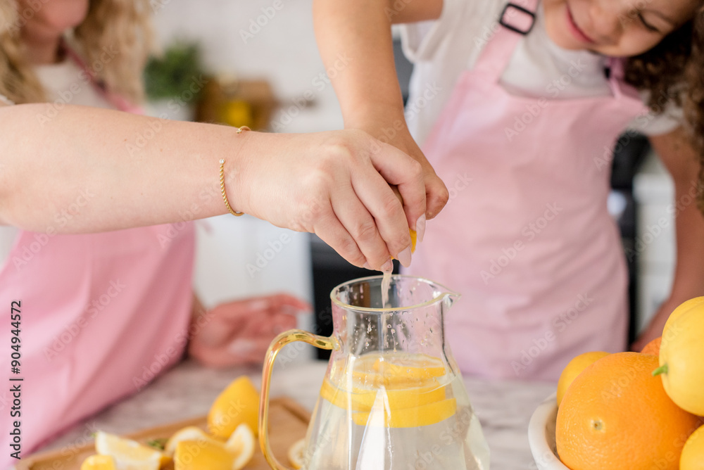 Close up of Mother and daughter squeezing a lemon in the pitcher Close up of Mother and daughter squeezing a lemon in the pitcher