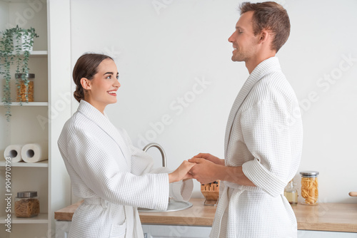 Couple in bathrobes holding hands in kitchen, morning routine and relationshi...