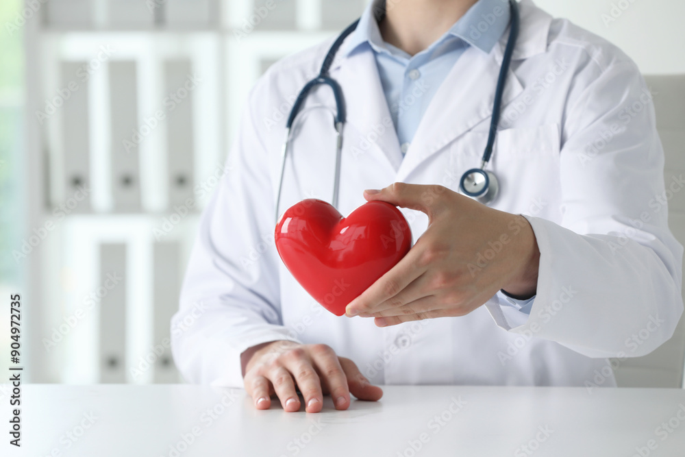 Doctor with red heart at white table in clinic, closeup Doctor with red heart at white table in clinic, closeup