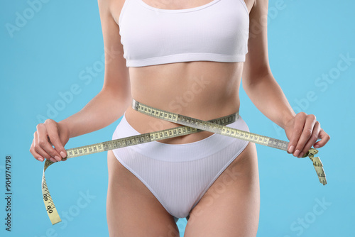 Diet and weight loss concept. Woman with measuring tape showing her slim body against light blue background, closeup