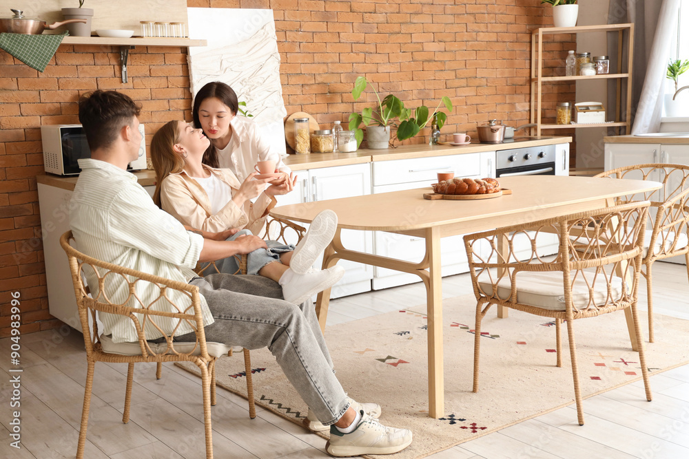 custom made wallpaper toronto digitalYoung man with two women kissing in kitchen. Polyamory concept