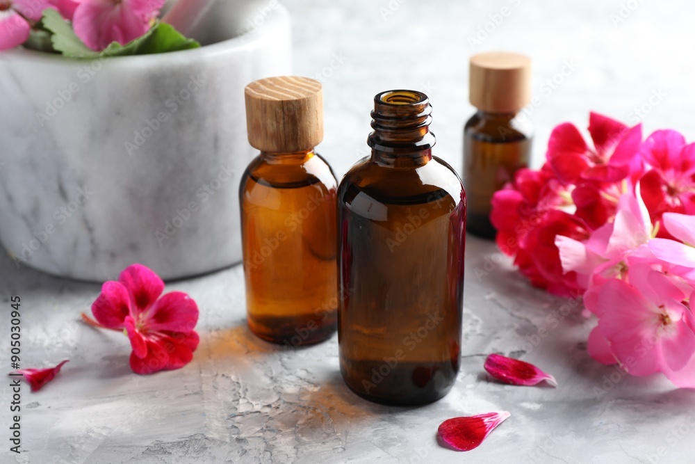 Bottles of geranium essential oil and beautiful flowers on light grey textured table, closeup Bottles of geranium essential oil and beautiful flowers on light grey textured table, closeup