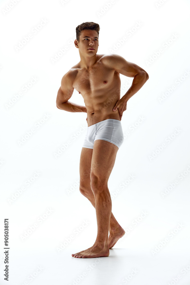 Fototapeta premium Young handsome man with athletic physique posing naked in boxers shows his tanned body against white studio background. Concept of body care, male health, natural beauty, youth, masculinity. Ad