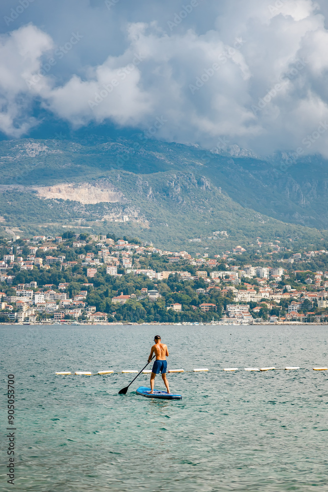Naklejka premium Man paddle boarding in the sea near the city with mountains in background