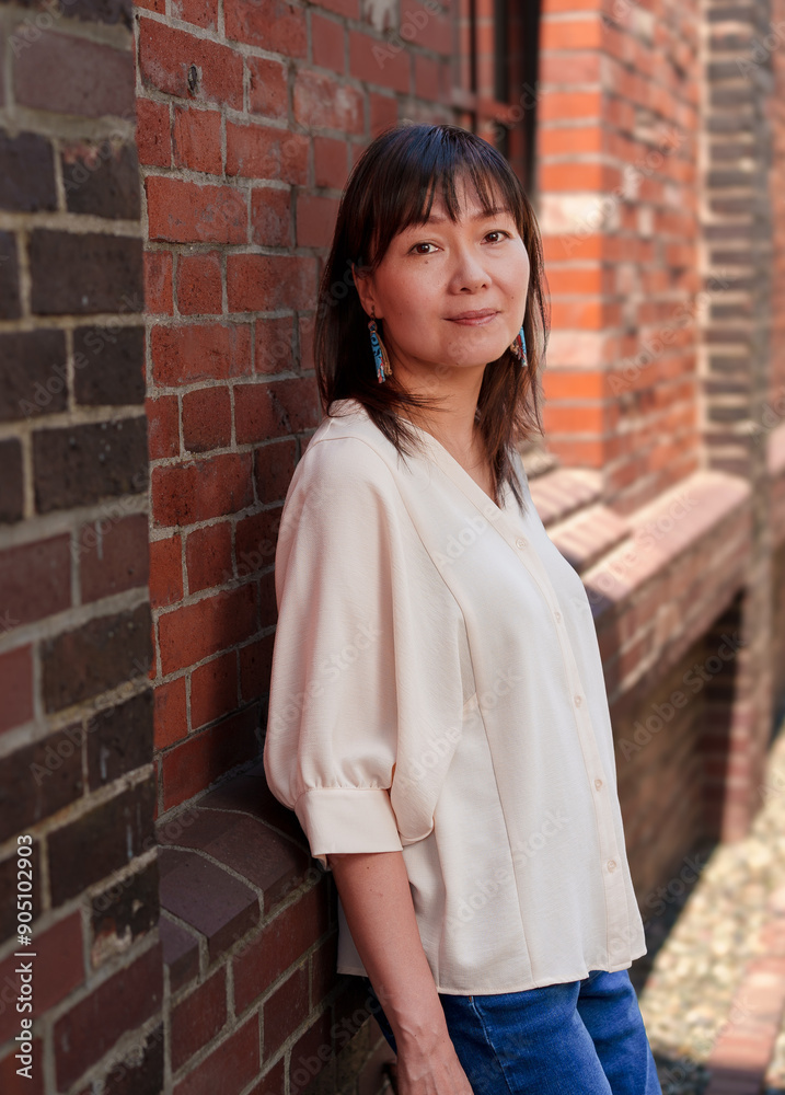 Fototapeta premium 煉瓦の壁に寄りかかってこちらを向く女性