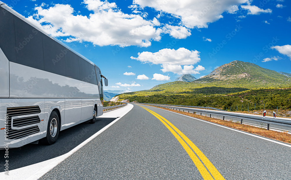 A white tourist bus travels along a picturesque mountain road.