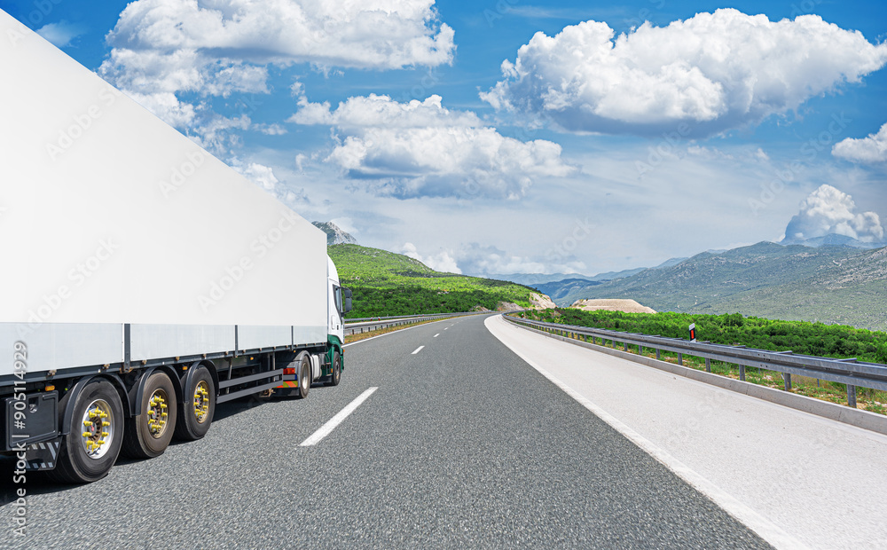 A white truck transports cargo along the highway against the backdrop of a mountain landscape.