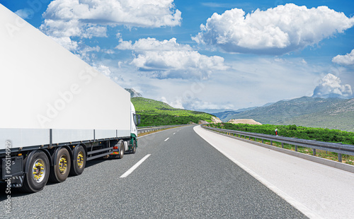 Obraz na płótnie A white truck transports cargo along the highway against the backdrop of a mountain landscape. w salonie