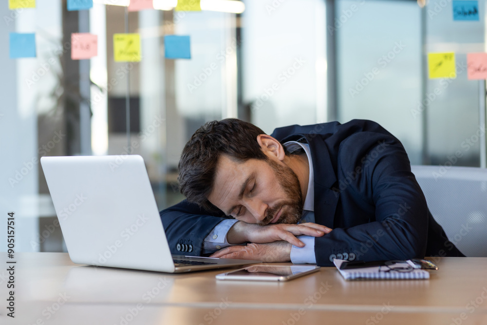 Exhausted businessman in suit sleeping on desk beside laptop and documents in modern office. Concept of workplace fatigue, overwork, stress, and work-life balance among office workers. Exhausted businessman in suit sleeping on desk beside laptop and documents in modern office. Concept of workplace fatigue, overwork, stress, and work-life balance among office workers.