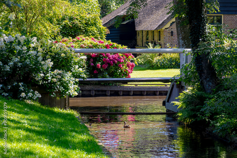 Selective focus of old wooden bridge crossing the canal in a small town in summer, Giethoorn is a mostly car-free village in the northeastern Dutch province of Overijssel, Steenwijkerland, Netherlands Selective focus of old wooden bridge crossing the canal in a small town in summer, Giethoorn is a mostly car-free village in the northeastern Dutch province of Overijssel, Steenwijkerland, Netherlands