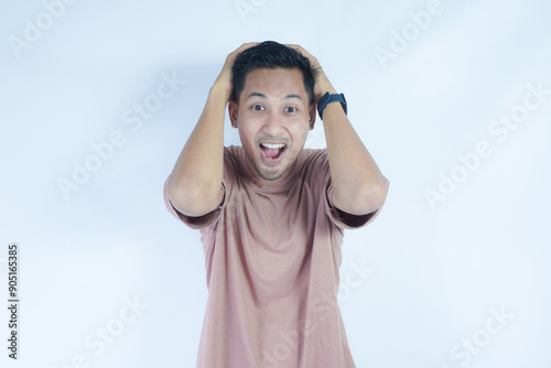 Shock content. Surprised young male in pink t-shirt shouting, holding his head with both hands