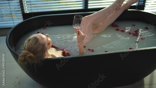 Spa relaxation. Woman lying in bath with holding glass with red wine. Girl relaxing in bathroom at home. Pretty female taking hot bath drinking wine. Stress relief. Rest after hard working day