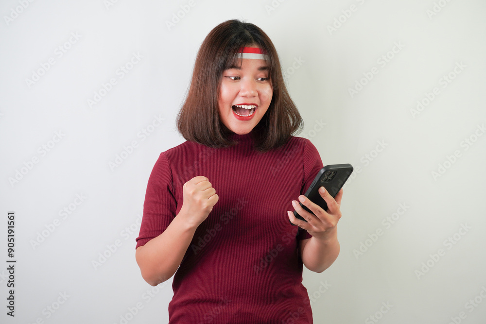 Surprised shocked young asian woman wearing Indonesian Flag headband is watching vertical smartphone screen for advertising, isolated over white background. Indonesian Independence Day. Surprised shocked young asian woman wearing Indonesian Flag headband is watching vertical smartphone screen for advertising, isolated over white background. Indonesian Independence Day.