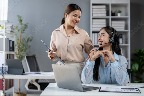 Two women are sitting at a desk with a laptop and a clipboard