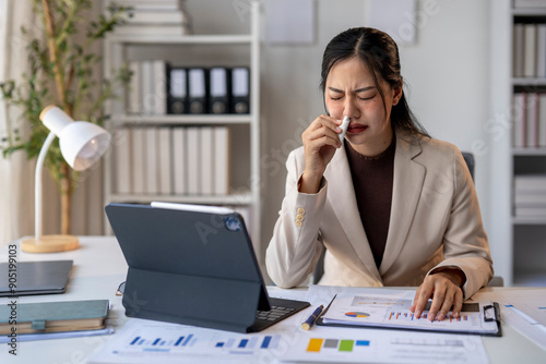 A woman is sitting at a desk with a laptop and a stack of papers