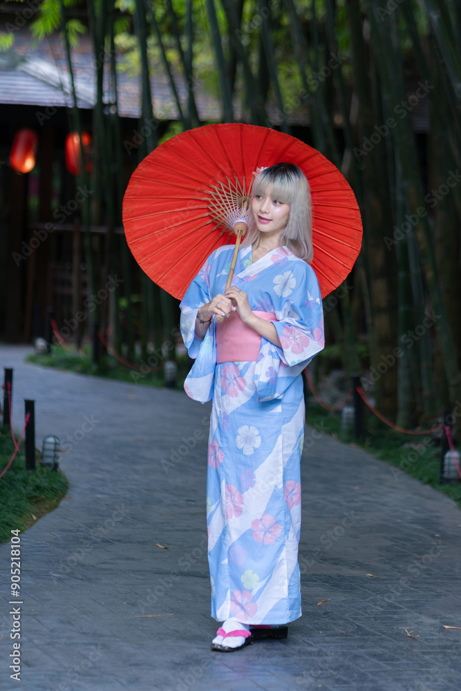 Fototapeta premium Pretty girl in a Yukata dress. A young Asian woman wearing a traditional Japanese kimono or Yukata dress is happy and relaxing with beautiful red maple leaves on the ground in the park.