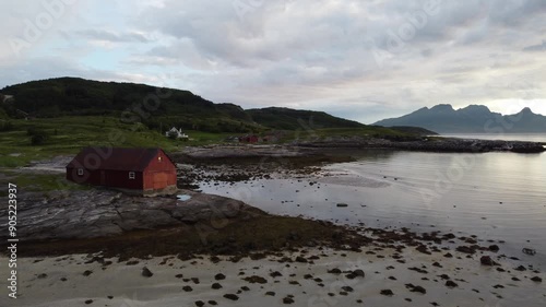 Red wooden hut cabin on a Northern Norway beach during midnight sun in summer with reflection on water
