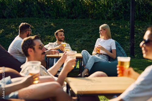 Sticker Positive young men and women,friends gathering outdoors in public place, enjoying company, conversation and beer
