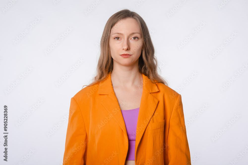 Confident young woman wearing an orange blazer looking at camera, posing on a white studio background
