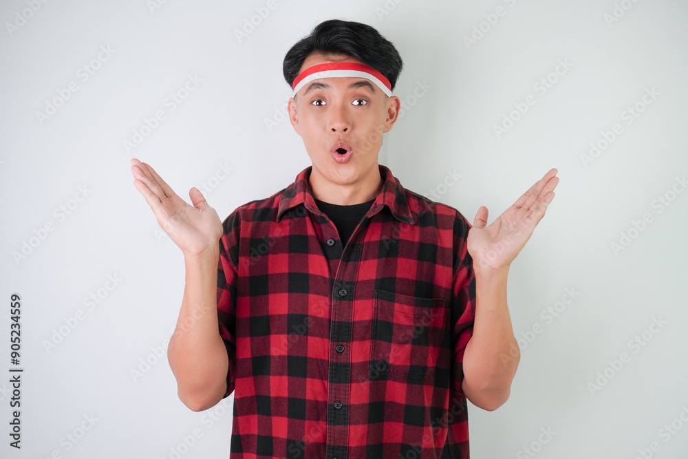 Surprised young asian man wearing Indonesian flag headband, amazed expression with hands open gesture, isolated over white background. Concept for Indonesian Independence Day. Surprised young asian man wearing Indonesian flag headband, amazed expression with hands open gesture, isolated over white background. Concept for Indonesian Independence Day.