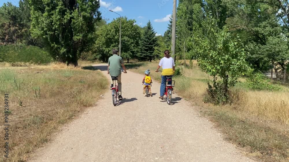 Family bike ride in the park. Mother with two sons riding bicycles on the path in summer. Simferopol, Crimea Family bike ride in the park. Mother with two sons riding bicycles on the path in summer. Simferopol, Crimea
