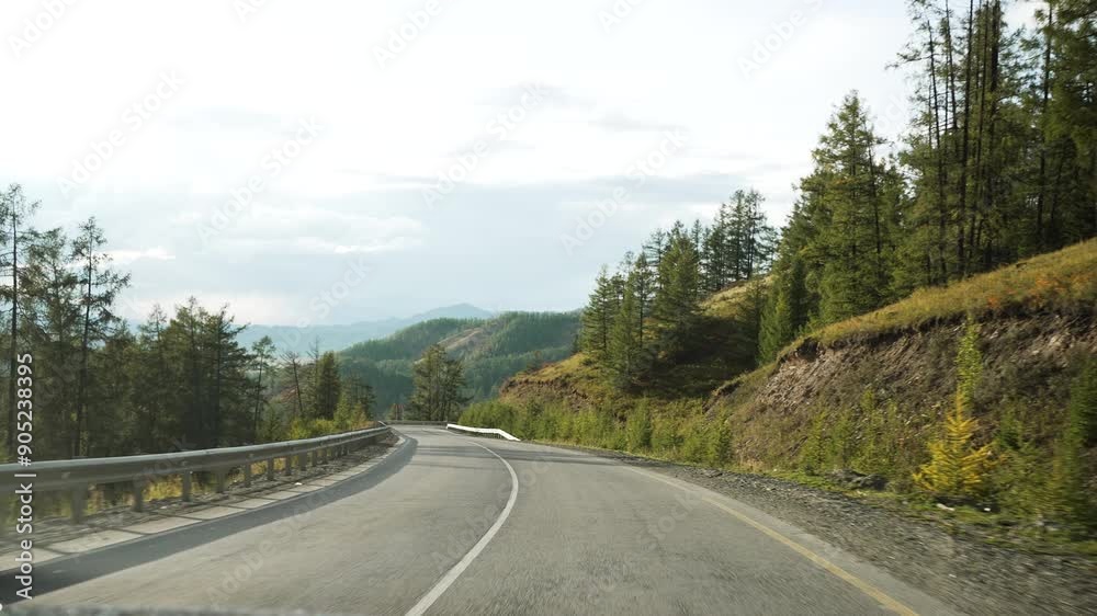 Winding mountain road with safety barriers offers scenic views of lush forests and distant hills under a cloudy sky. Car travel, adventure on the road, first-person view. Winding mountain road with safety barriers offers scenic views of lush forests and distant hills under a cloudy sky. Car travel, adventure on the road, first-person view.