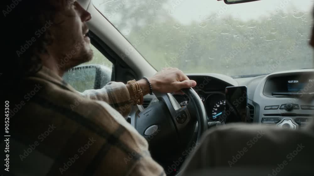 Medium close-up rear shot of young Caucasian man and woman driving in car together in pouring rain, on way to vacation, having lively conversation, looking at each other and smiling Medium close-up rear shot of young Caucasian man and woman driving in car together in pouring rain, on way to vacation, having lively conversation, looking at each other and smiling