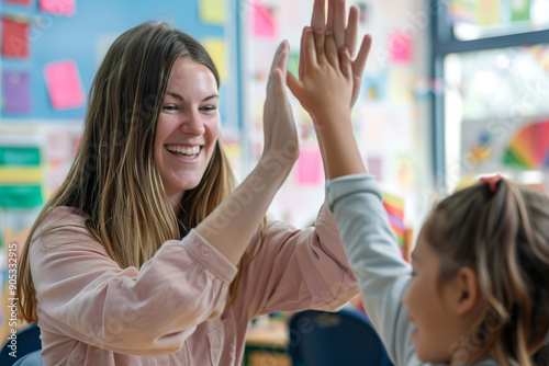 A happy elementary school teacher gives a high-five to a smiling student during class.