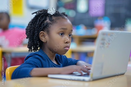 A little girl focuses intently as she e-learns on a laptop in her elementary school computer science classroom.