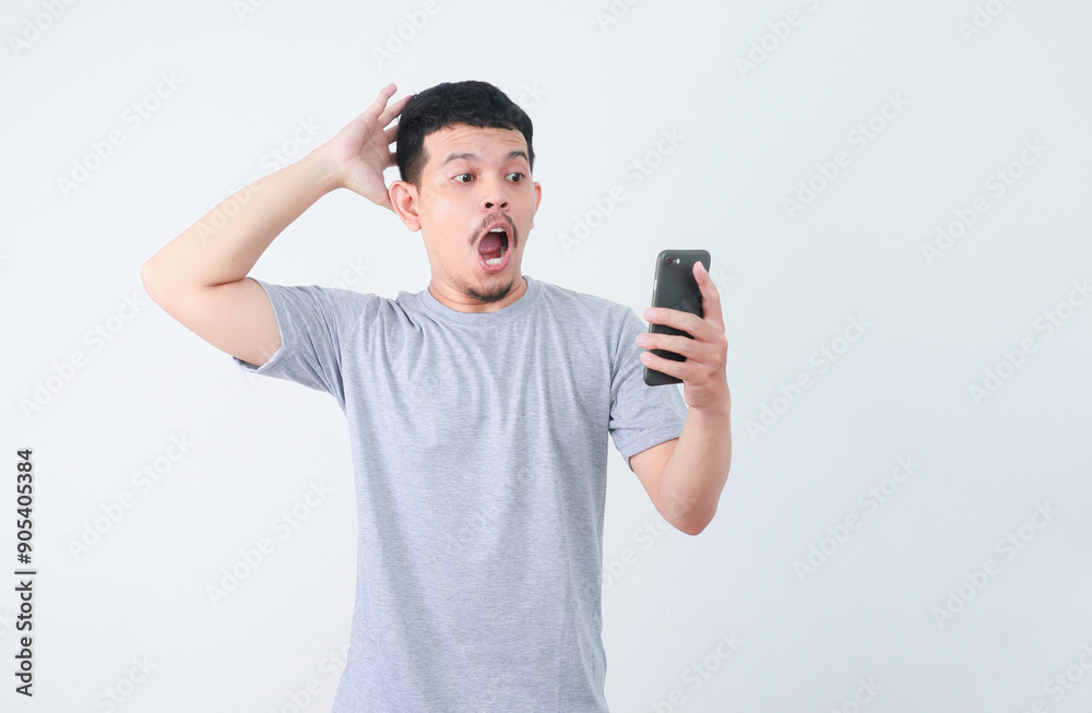 Asian man holding mobile phone and feeling shocked portrait white isolated Asian man holding mobile phone and feeling shocked portrait white isolated