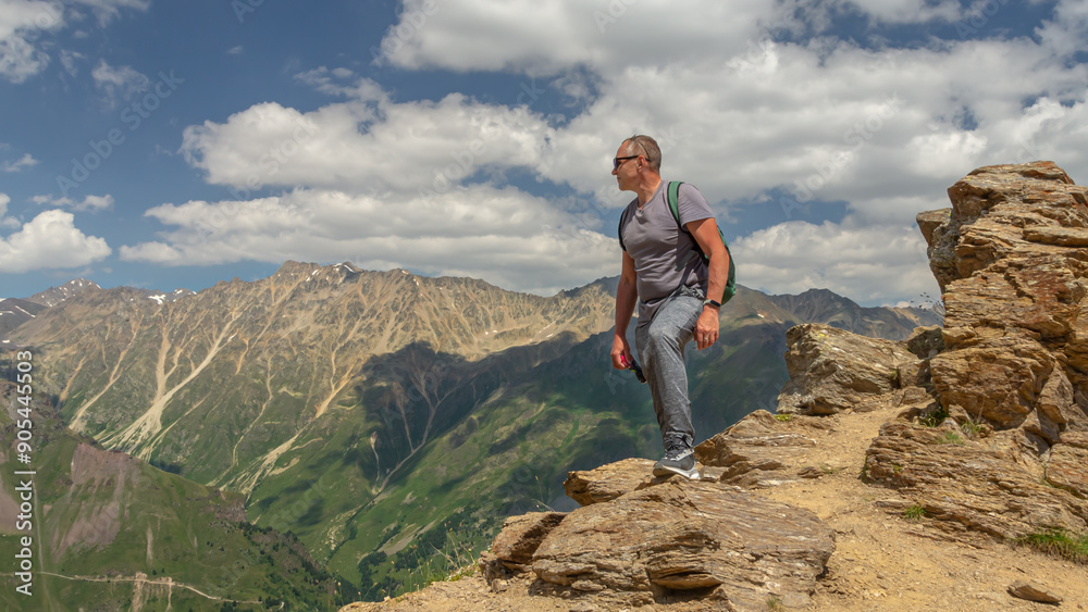Fototapeta premium A man looks at the high snow-capped mountains. The conquest of the mountains. The rocks are located high in the mountains. The nature of the highlands.