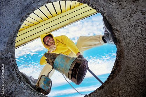 Man immerses waste pump into wastewater through hole in concrete well ring, seen from below.