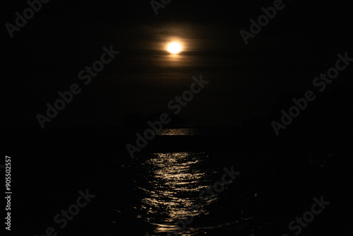 full moon reflected in the sea on a dark night warm light