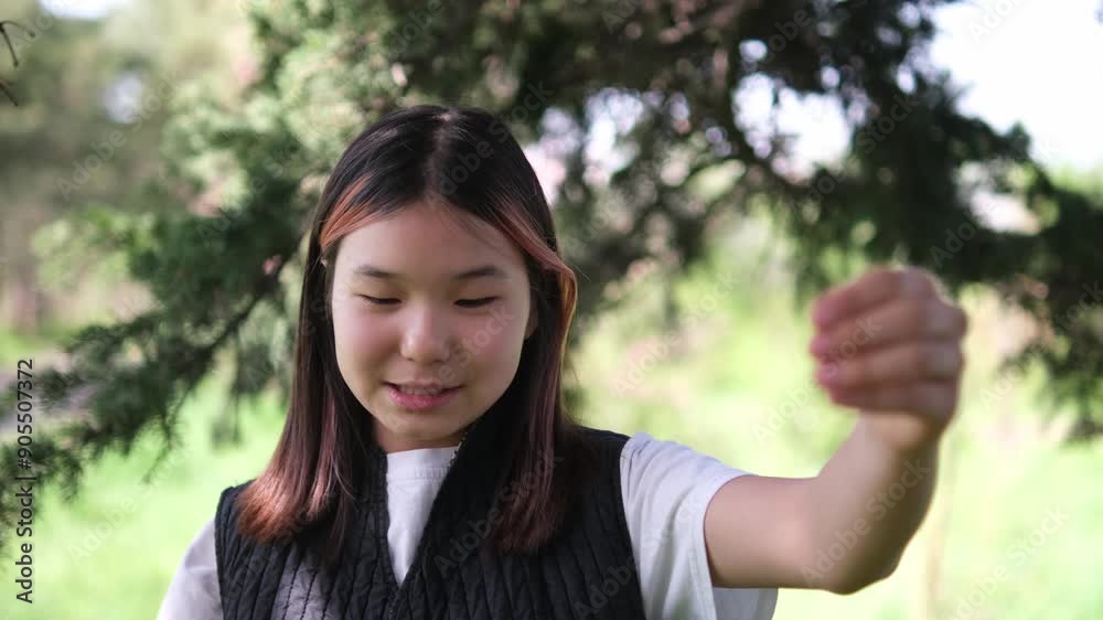 Asian girl smiling playfully and telling something in the park. having great time in the park during summer vacation, with lush green grass and trees in background Asian girl smiling playfully and telling something in the park. having great time in the park during summer vacation, with lush green grass and trees in background