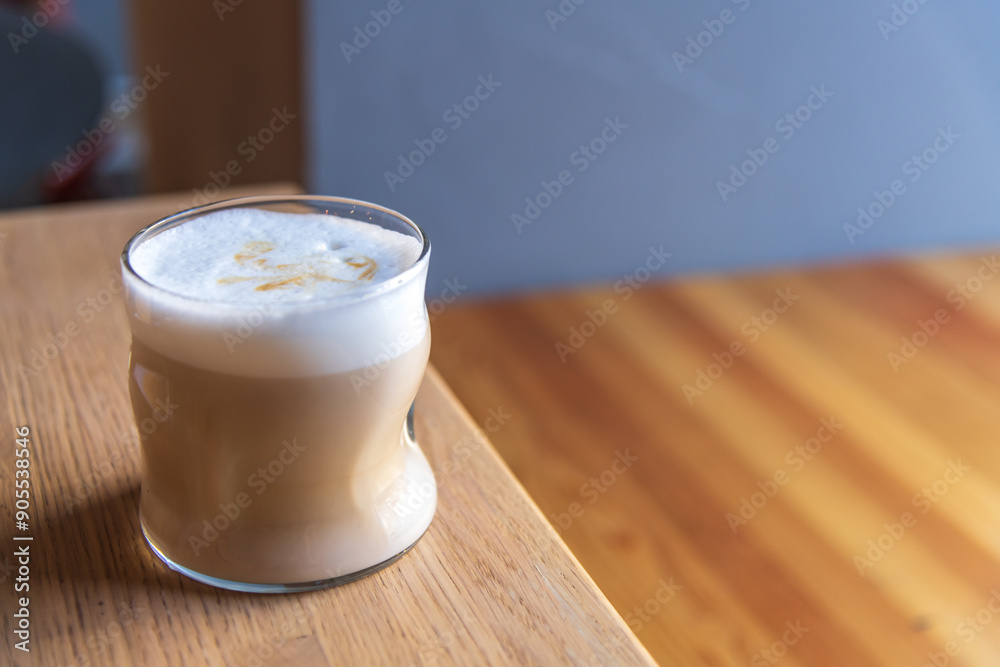 Close-up side view of drinking glass with latte macchiato standing on wooden table in cafe or restaurant. Copy space. Soft focus. Coffee beverages theme. Close-up side view of drinking glass with latte macchiato standing on wooden table in cafe or restaurant. Copy space. Soft focus. Coffee beverages theme.