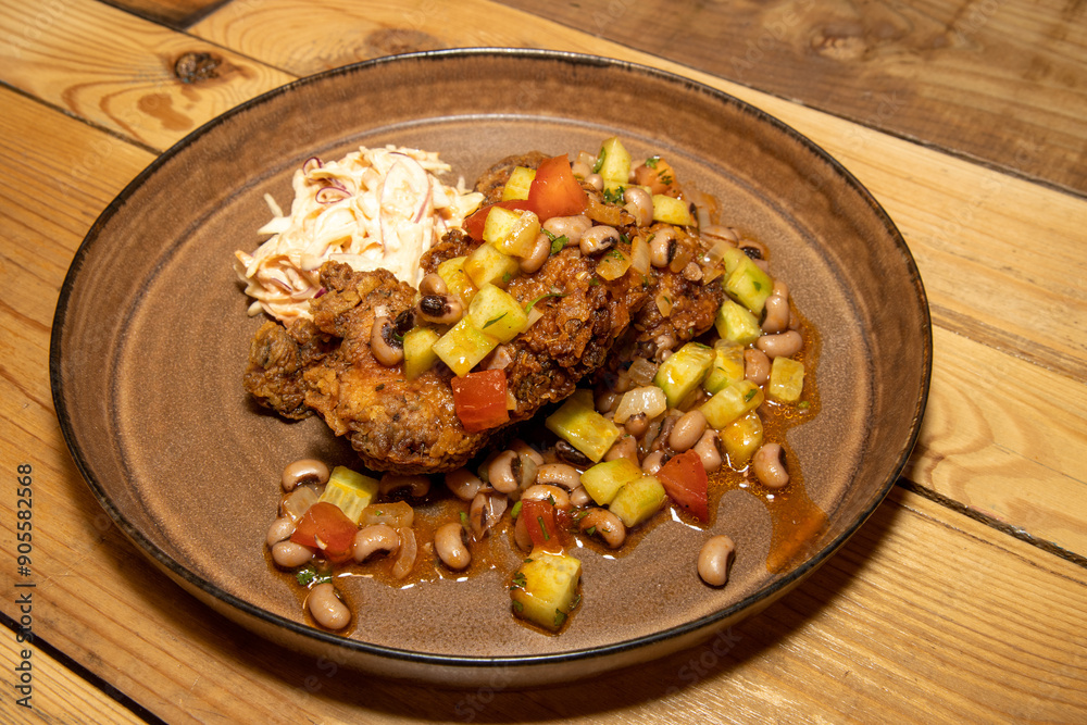 A delicious plate of home made fried chicken with beans and cut vegetables on a wooden kitchen table