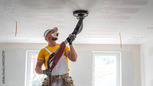 The worker sanding a plasterboard ceiling. He is using special drywall sander. A red plasterboard improve the fire resistance of ceiling structures. photo