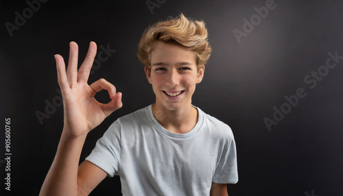 Smiling blonde teenager showing OK sign on black background