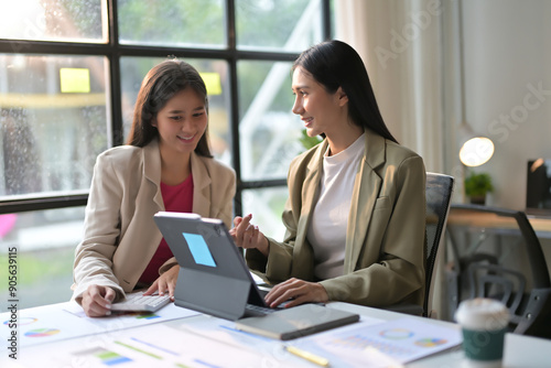 Two Businesswomen Collaborating on a Project in a Modern Office with Laptops and Documents © PaeGAG