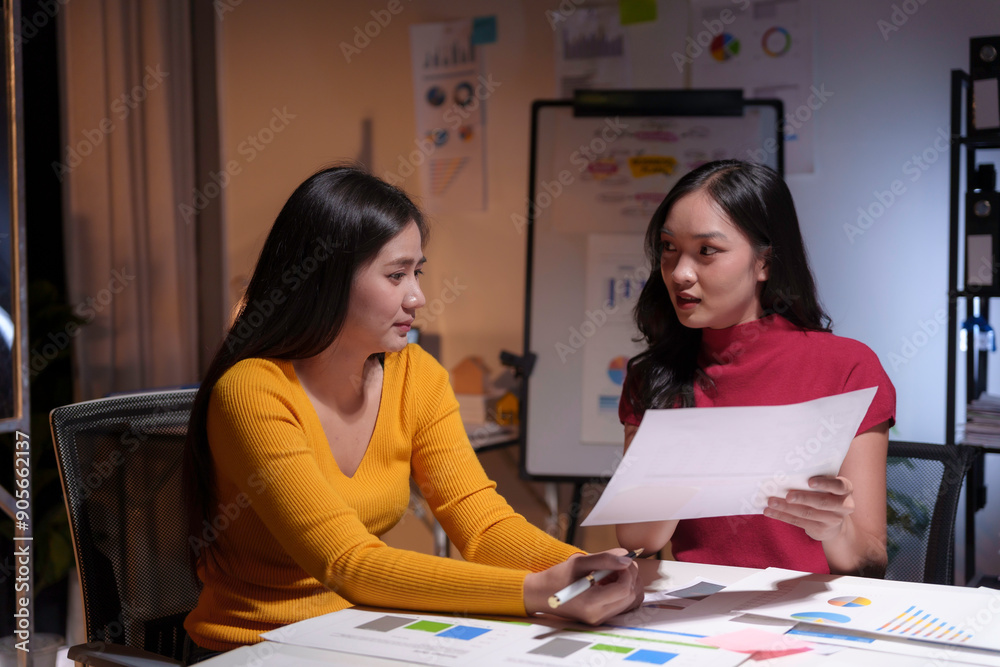 Two businesswomen working late in office having business discussion about financial report Two businesswomen working late in office having business discussion about financial report