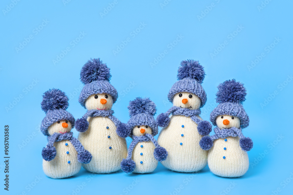 Family of knitted snowmen celebrate the holidays on blue background. Winter fairy tale story with your own hands, hobby. Merry Christmas and New Year 2025 greeting card Family of knitted snowmen celebrate the holidays on blue background. Winter fairy tale story with your own hands, hobby. Merry Christmas and New Year 2025 greeting card