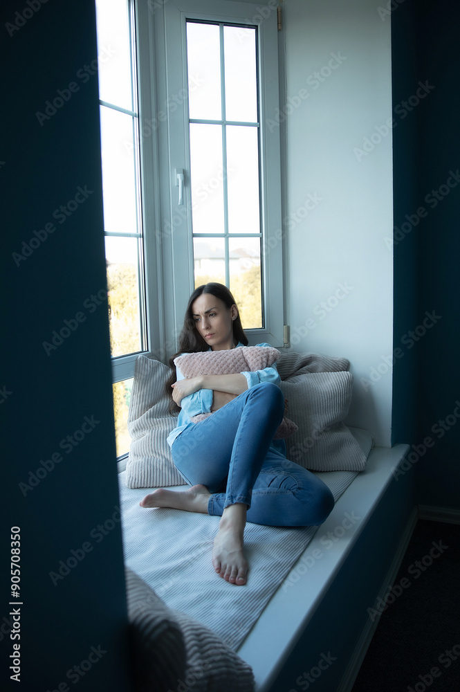 Sad, depressed, frustrated, angry, lonely, emotional young woman with severe stress and mental problem, disease, headache, illness, divorce, victim of violence. Female sitting on big window sill Sad, depressed, frustrated, angry, lonely, emotional young woman with severe stress and mental problem, disease, headache, illness, divorce, victim of violence. Female sitting on big window sill
