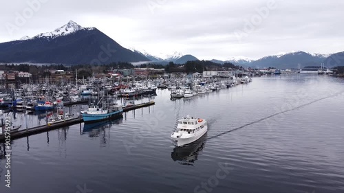 Aerial view of boat leaving harbour Sitka, Alaska, late winter snowcapped mountains and cold ocean. Cinematic drone video