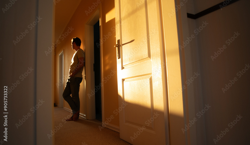 Fototapeta premium Side view photo of young confident man at home in corridor while he leaning on wall with sundown on background