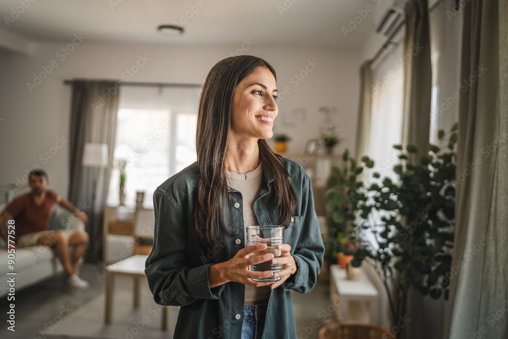 Portrait of adult women stand, hold glass of water look out the window