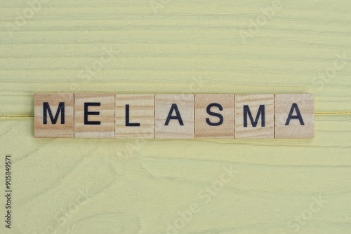  the gray word melasma of gray small wooden letters lie on a yellow table photo