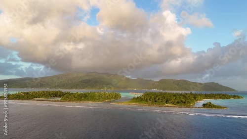 Aerial view captured by drone of small motu islands near Taha'a in French Polynesia. The motus are covered with dense palm trees and surrounded by beautiful ocean water. 