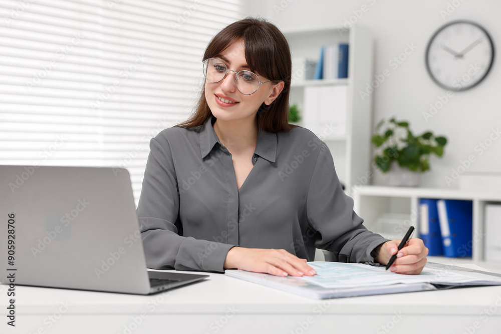 Smiling secretary doing paperwork at table in office Smiling secretary doing paperwork at table in office