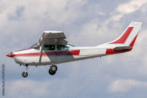 Unmarked and generic high wing general aviation aircraft.  Red stripe on white paint of a piston powered propeller driven airplane on approach to landing