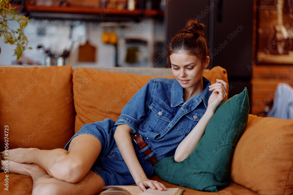 Obraz premium Woman relaxing on couch with book in hand wearing denim shirt in cozy living room setting concept